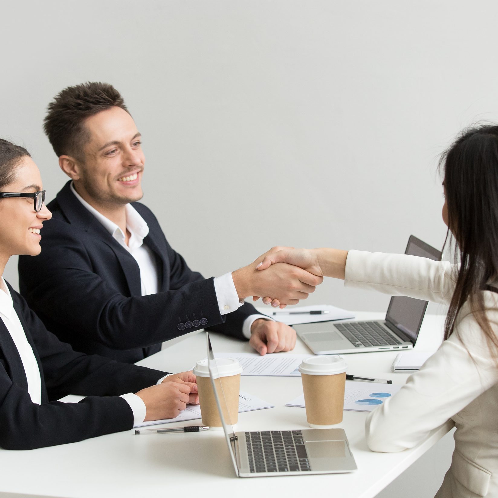 Friendly satisfied partners handshaking at group meeting thanking for successful teamwork, smiling millennial businessman shaking hand greeting businesswoman, respect or making contract deal concept